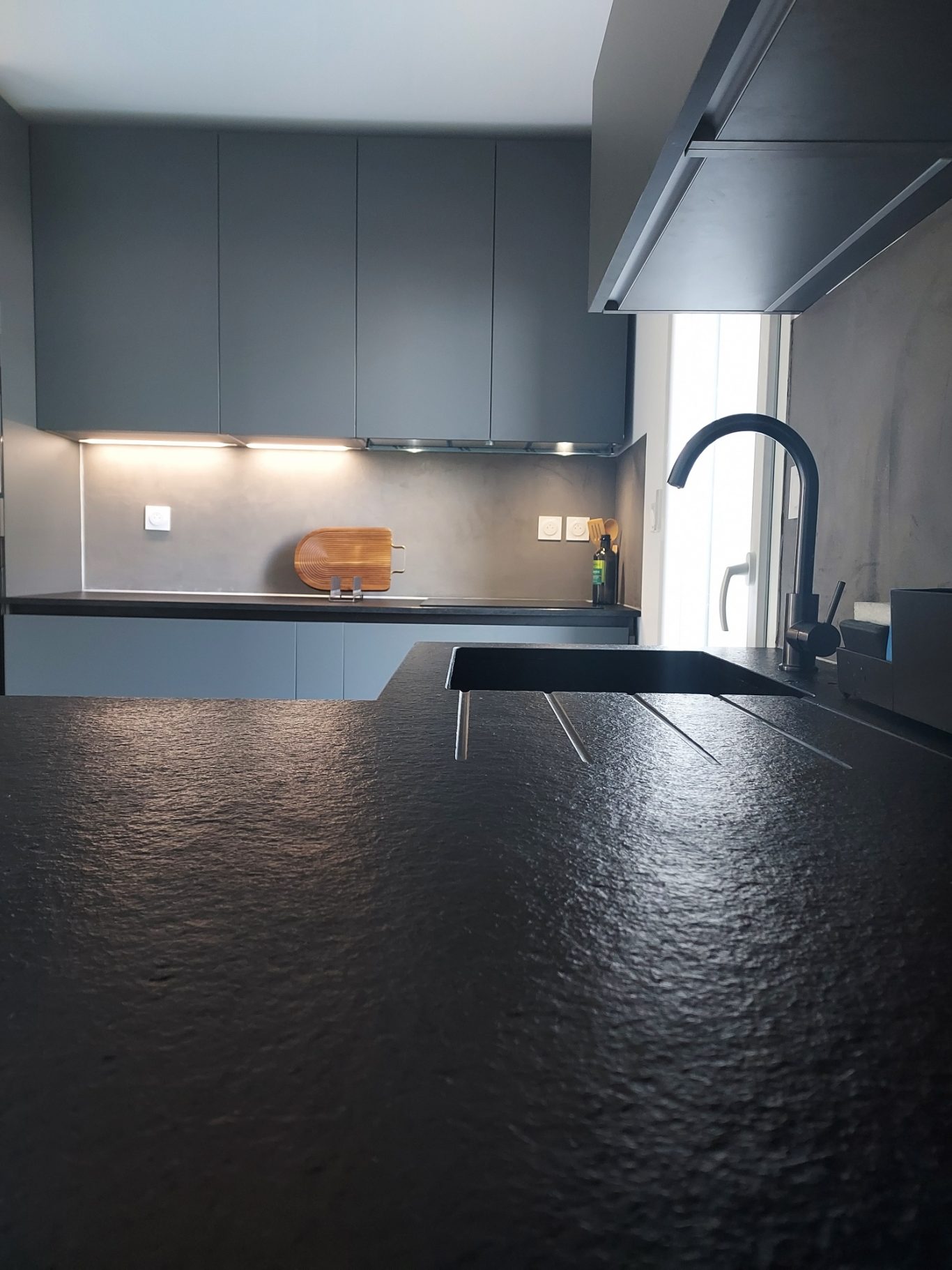 Plan de travail Cuisine moderne avec un comptoir noir, évier et arrière-plan lumineux.